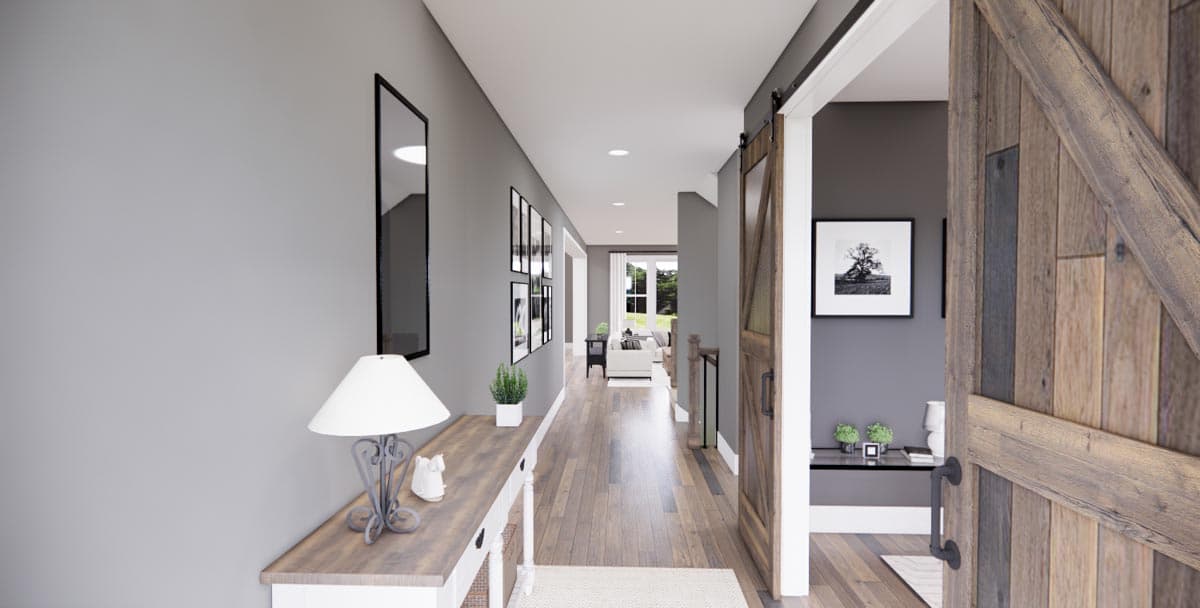 Interior view of a house plan, showing a hallway with a barn door, console table, and artwork leading to a living area.