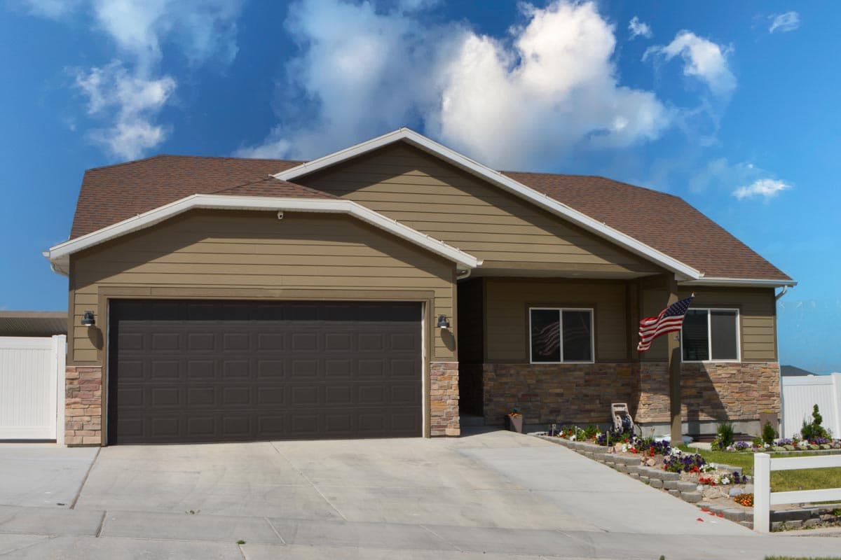 Ranch house plan exterior with a two-car garage, stone skirting, and prominent gables.
