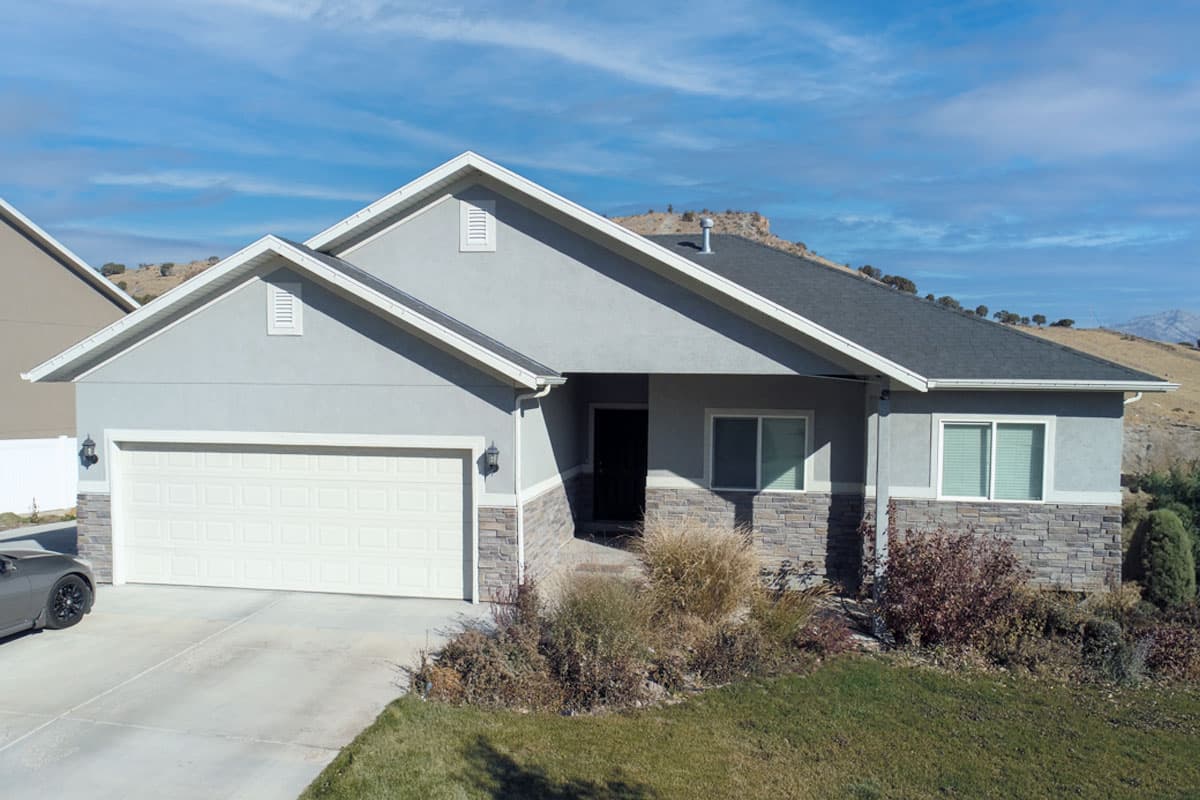 One-story house plan exterior with attached two-car garage, stone accent skirting, and multiple gables.
