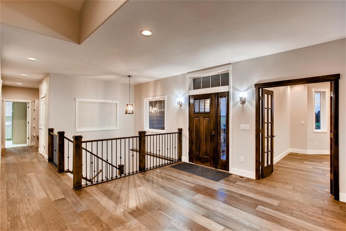 Interior view of a house with a wooden front door, staircase, and doorways to other rooms.