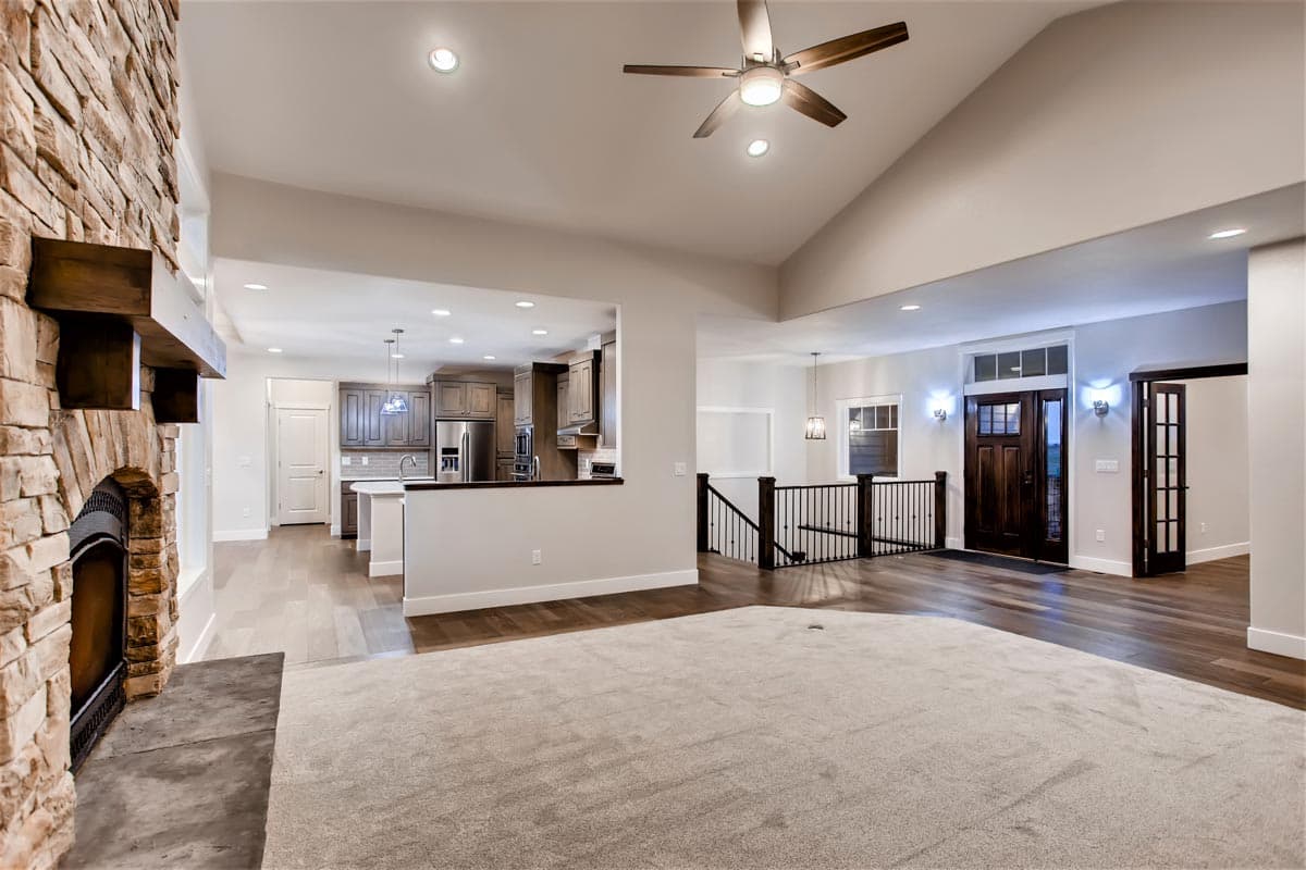 Great room with stone fireplace, vaulted ceiling, and open kitchen access. Features wood floors and stairs.