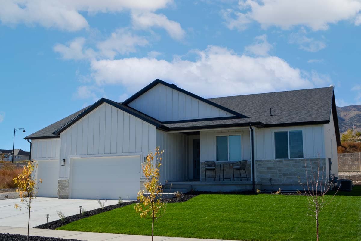 Modern Farmhouse house plan exterior with white vertical siding, stone accents, two-car garage, and covered porch.
