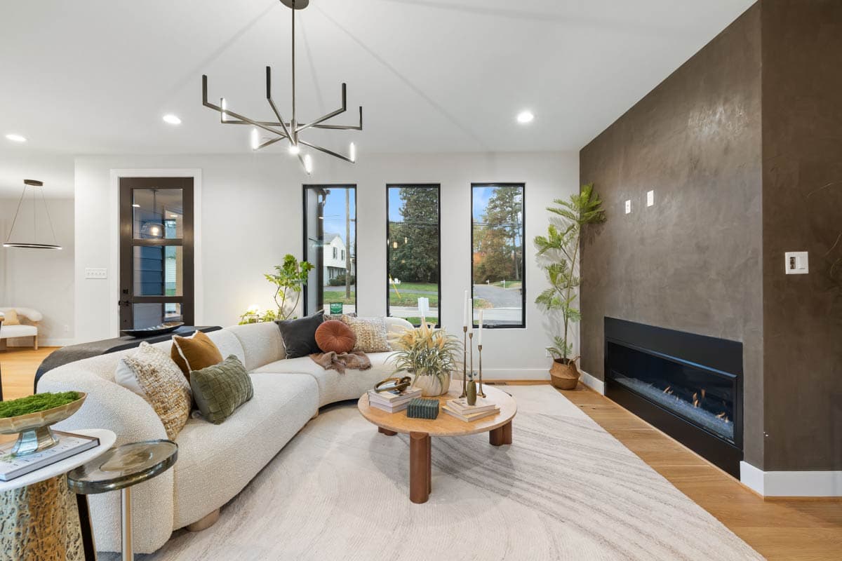 Modern living room featuring a curved off-white sofa with decorative pillows, a unique chandelier, and a fireplace with a textured brown accent wall.
