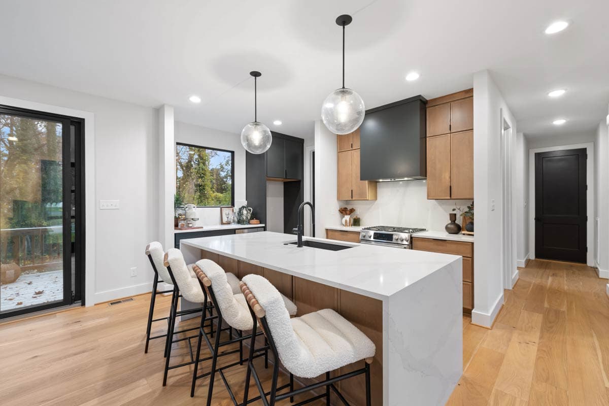Modern kitchen featuring a large island with white quartz countertop and furry bar stools. Globe pendant lights hang above the island.