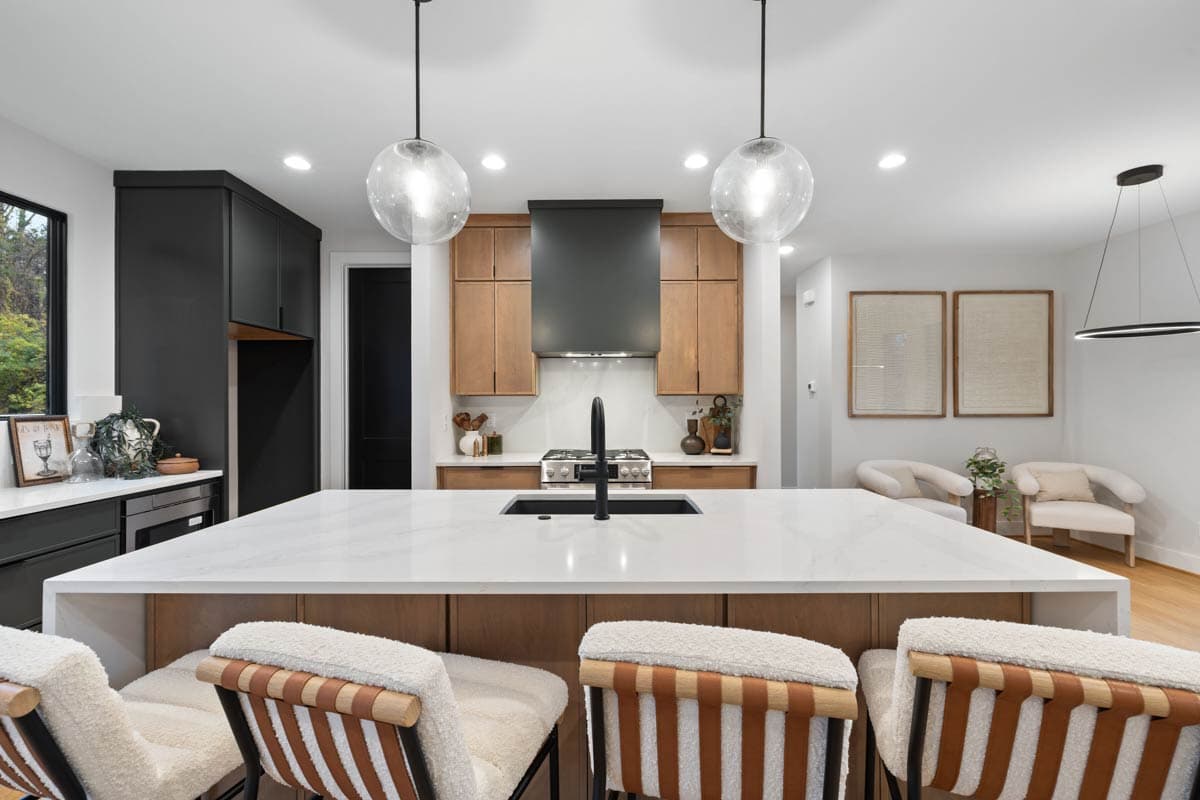 Modern kitchen with a large island and seating. Features include two globe pendant lights, dark cabinets, wooden cabinetry, and two armchairs.