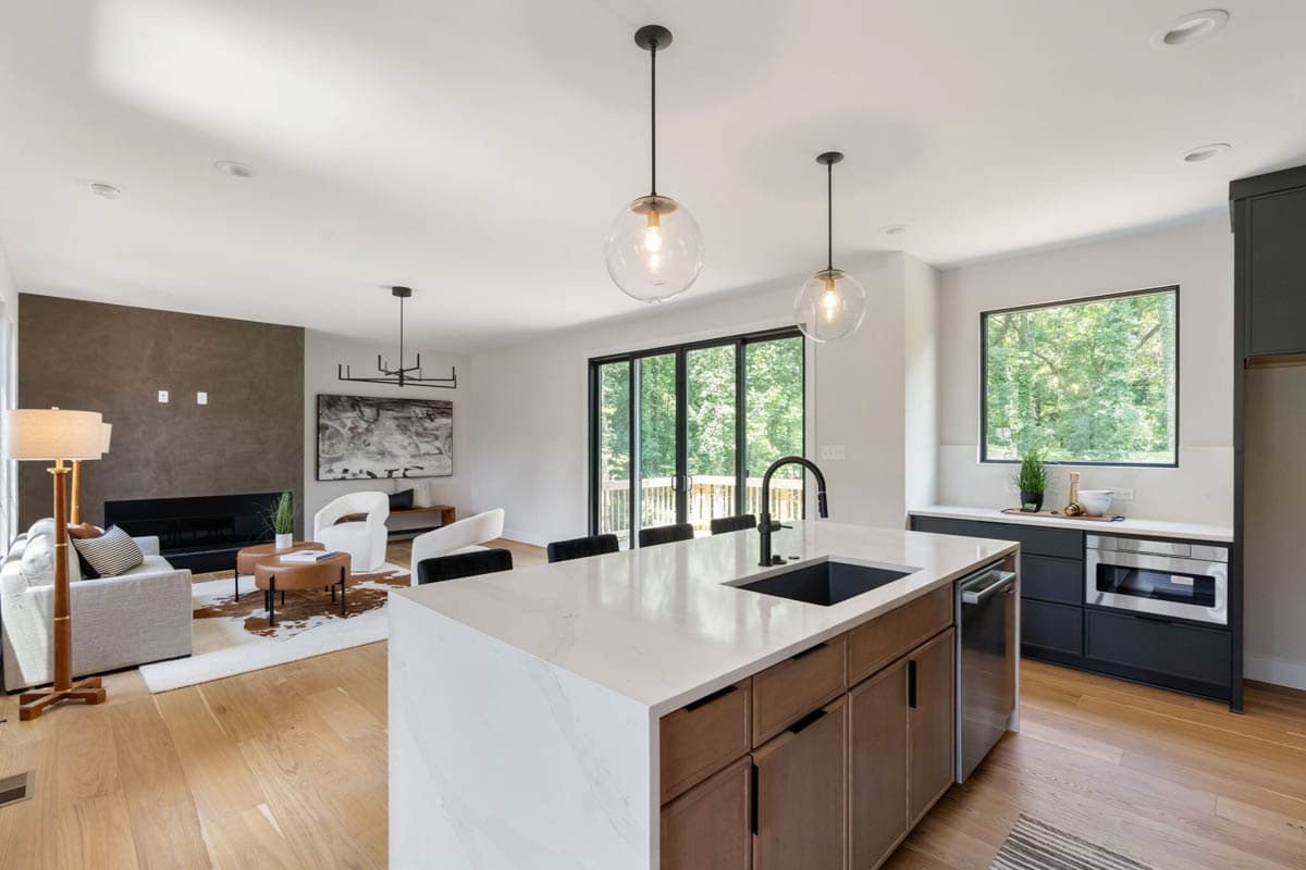 Modern, open-concept living space with a kitchen island, hardwood floors, and a living area with a fireplace and large windows.