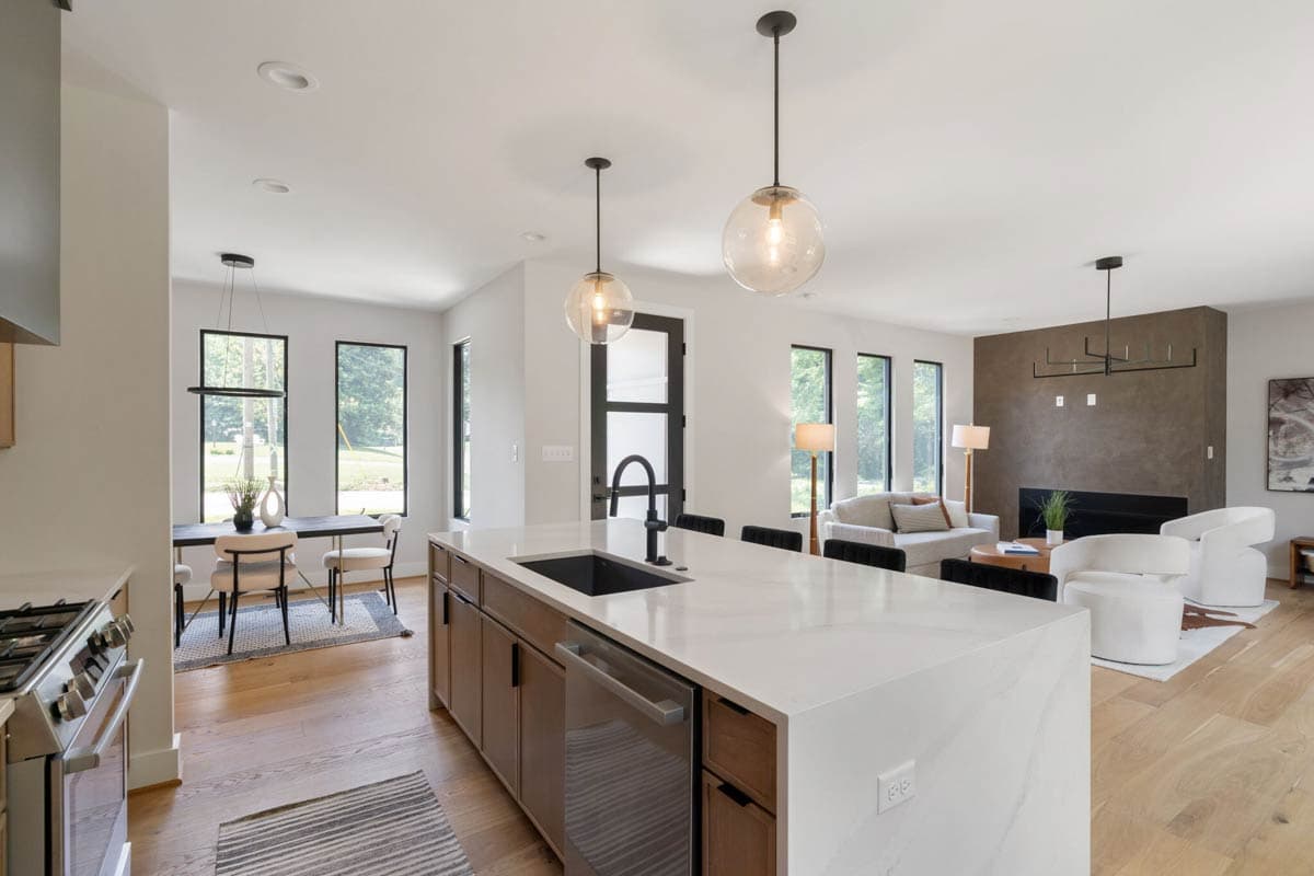 Modern open-plan living space with a kitchen island, dining area, and living room featuring a fireplace and large windows with outdoor views.