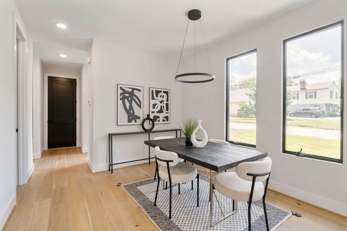 Modern dining room with a dark wood table, white chairs, and abstract art. Natural light streams in from large windows, showcasing neighborhood views.