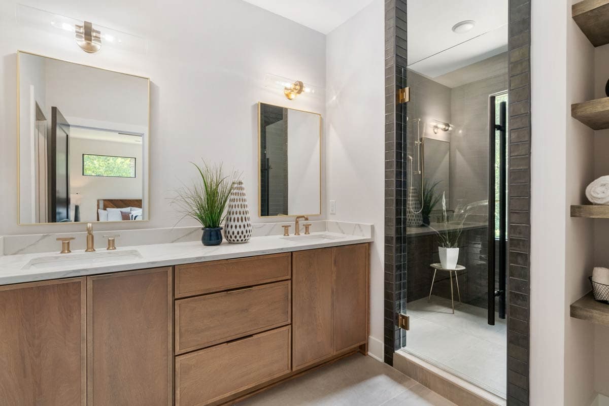 Modern bathroom with a double vanity, large mirrors, and a glass-enclosed shower. Decorative plants sit on the countertop and in the shower.