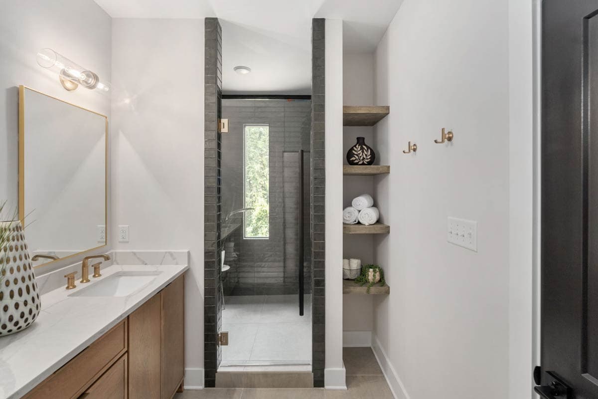 Modern bathroom featuring a vanity with gold accents, a walk-in shower, and a built-in shelving unit with decorative items and towels.
