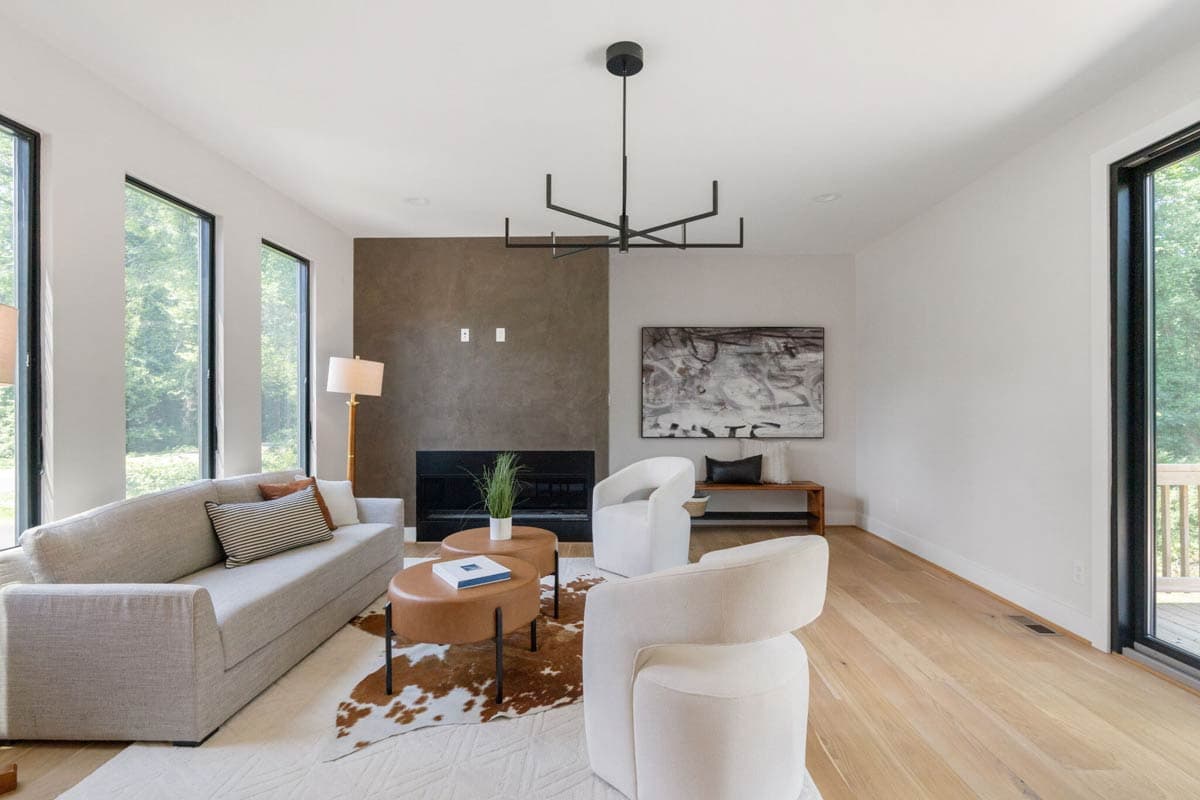 Modern living room with neutral tones, featuring a sofa, two white armchairs, a fireplace, and a cowhide rug. Large windows provide natural light.