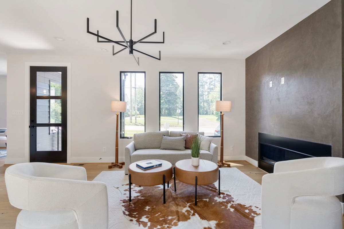 Modern living room with neutral tones, two white armchairs, a grey sofa, and a striking black chandelier. A cowhide rug adds a warm accent.