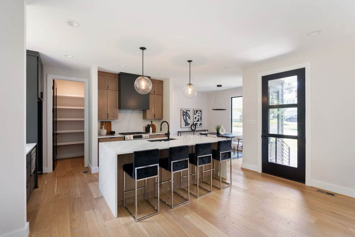 Modern open-concept kitchen with a large island, black velvet bar stools, and globe pendant lights over a marble countertop.
