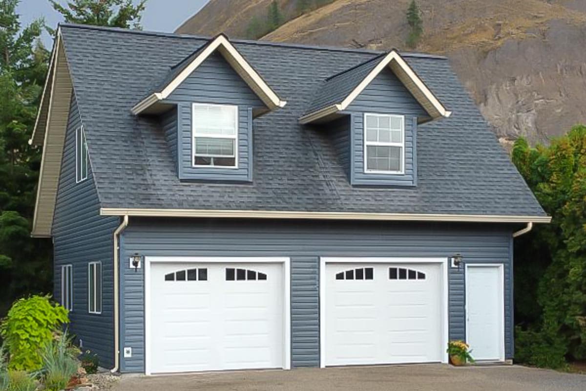 House plan exterior with two-car garage, dormers, and gabled roofline. Two stories with blue siding and white garage doors.