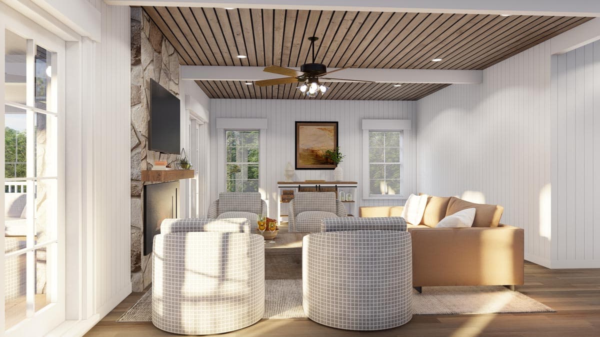 Living room with stone fireplace, wood-paneled ceiling, large windows, and light-colored sofa.