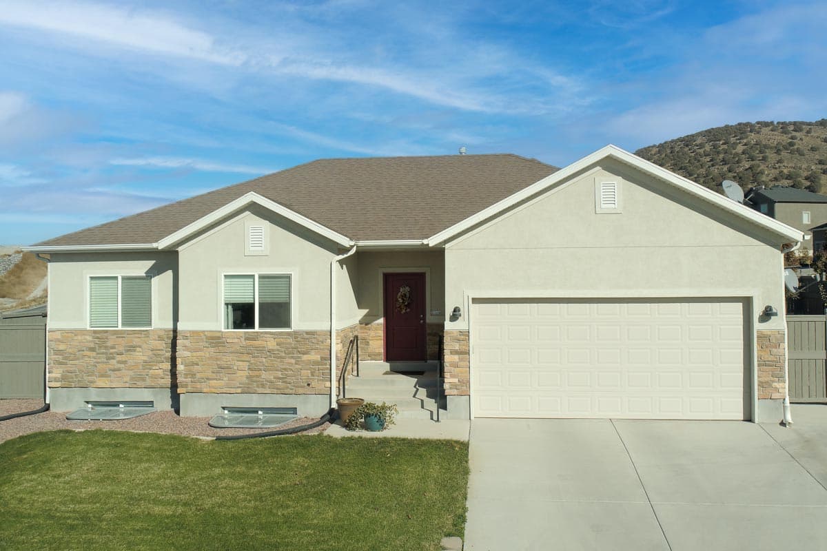 House plan exterior: One-story home with stone base, gable dormers, covered entry, and attached two-car garage.