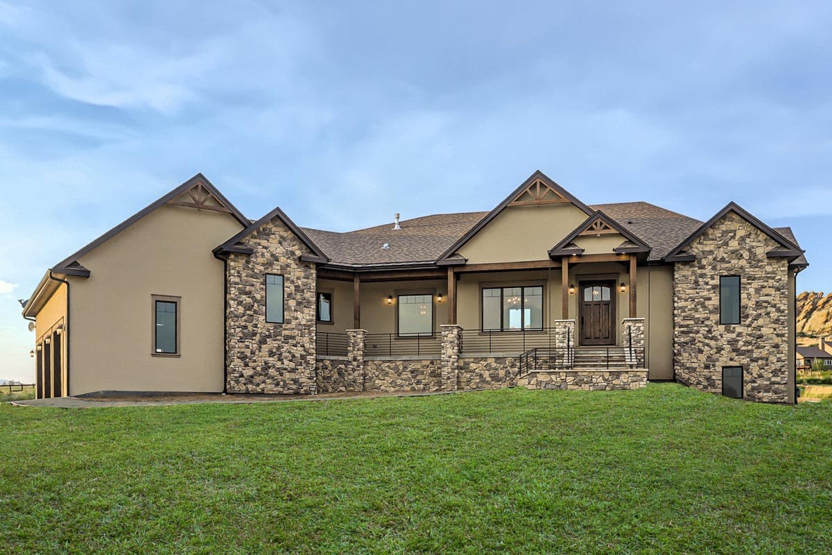 House plan exterior. Two-story home with stone accents, a covered porch, and gabled rooflines. Features a three-car garage and multiple windows.