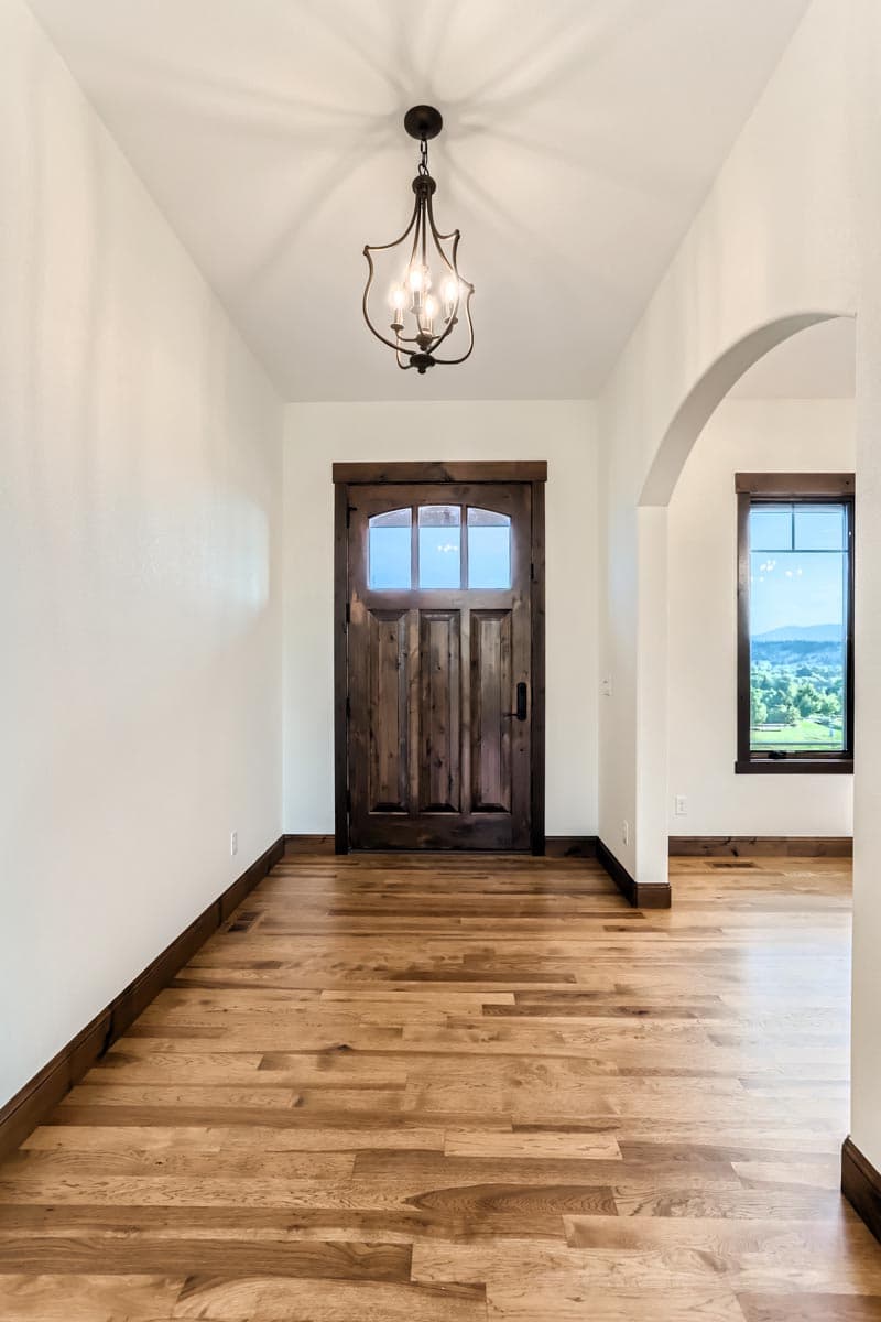 Interior view of entryway featuring a dark wood door with glass panes, archway, and hardwood floors.