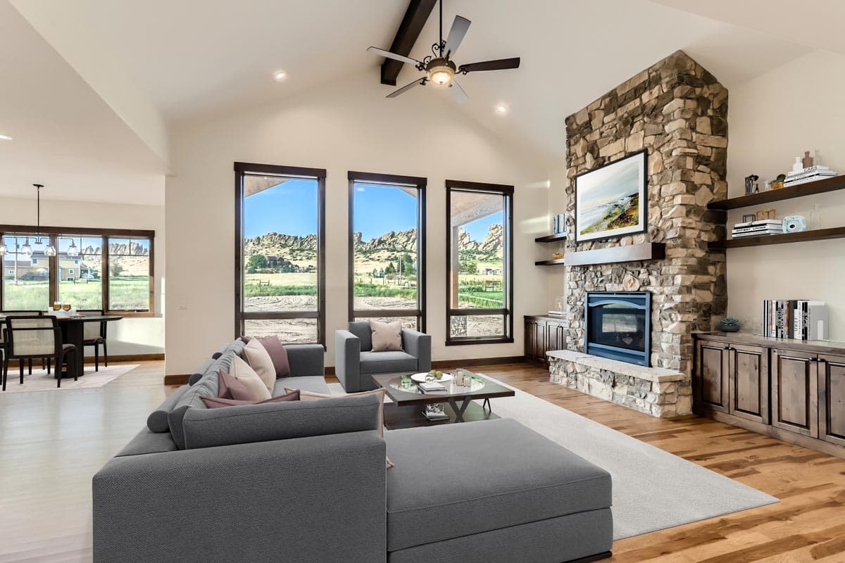 Living room with stone fireplace, vaulted ceiling with exposed beams, and large windows with mountain views. Dining area visible.