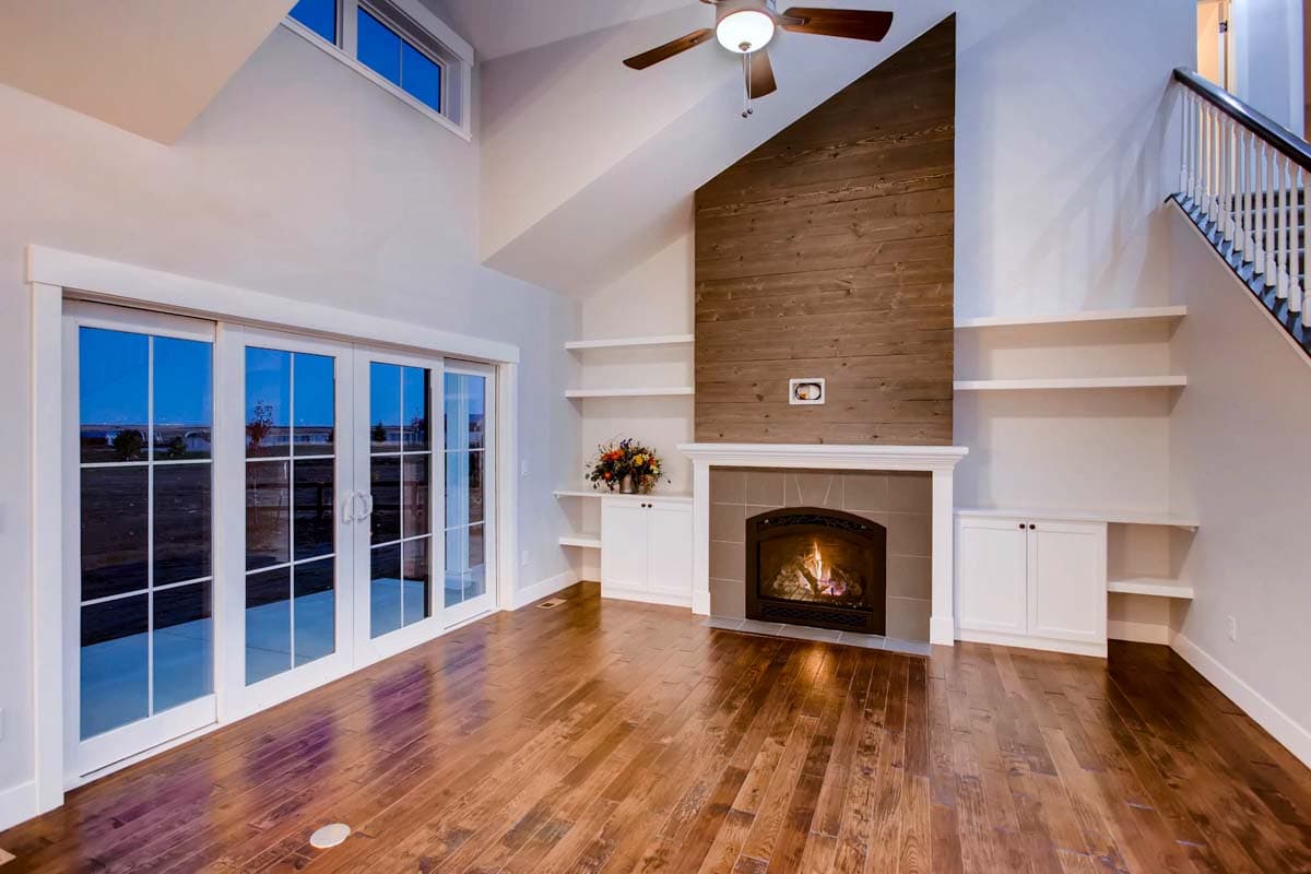 Great room with vaulted ceiling, wood-paneled fireplace, built-in shelving, and sliding glass doors.