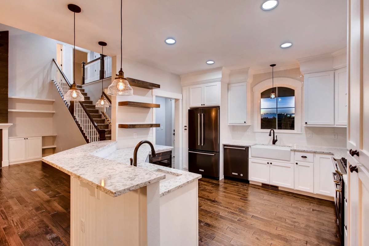 Kitchen with island, white cabinetry, farmhouse sink, stainless steel refrigerator, and staircase.
