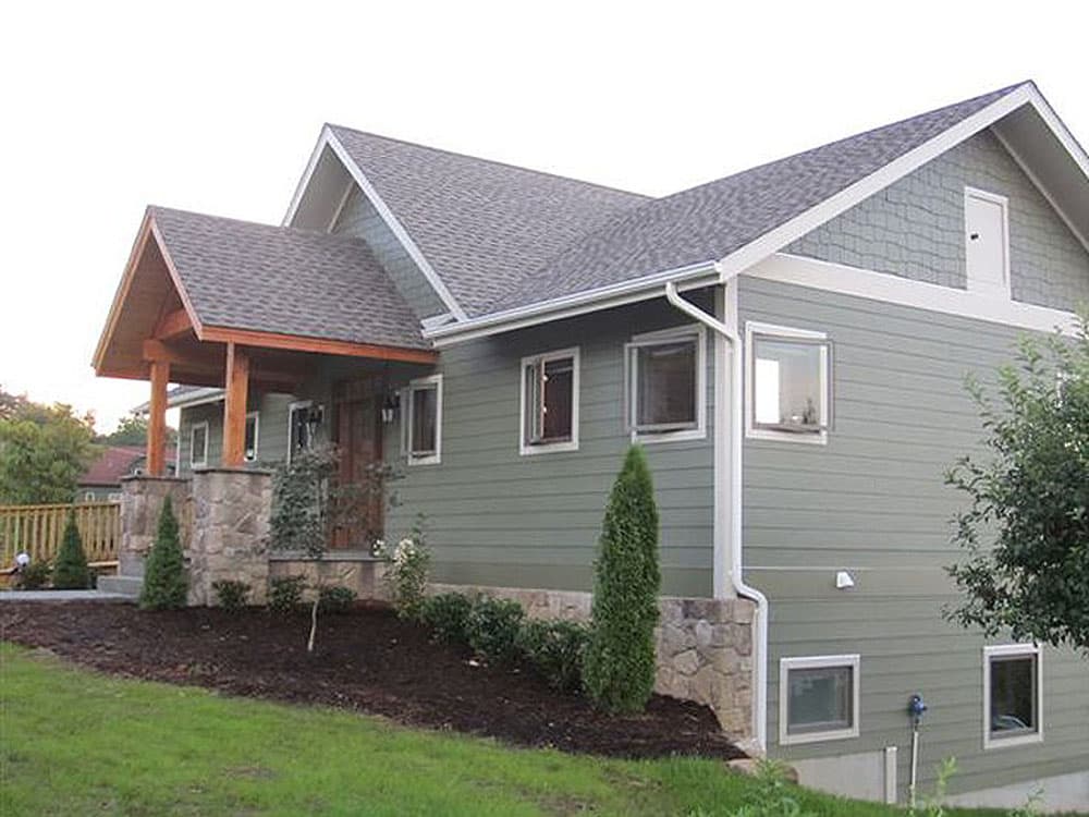 House plan exterior with gabled dormer, covered entry porch supported by stone pillars, and horizontal siding.