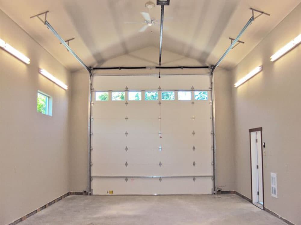 Garage interior with open overhead door, windows, and fluorescent lighting.
