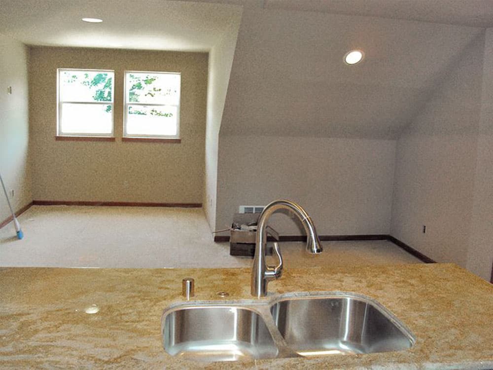 Interior view of unfinished room with double windows, angled ceiling, and double-basin sink on counter.