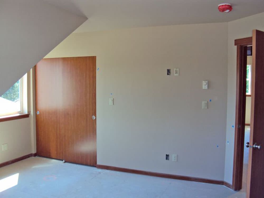 Interior view of a room with a large wooden sliding door, a window, and electrical outlets on the wall.