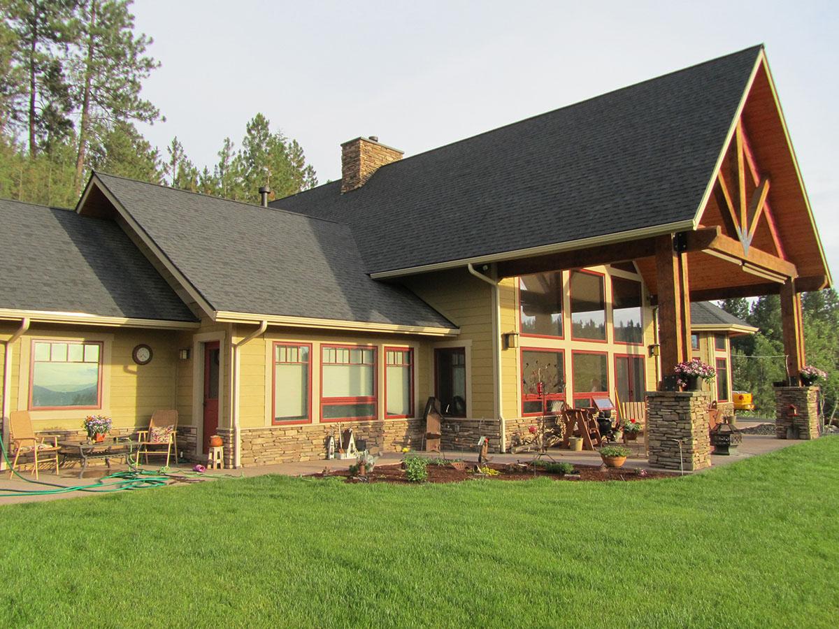 House plan exterior: single-story home with a covered porch, stone accents, gables, and large windows.