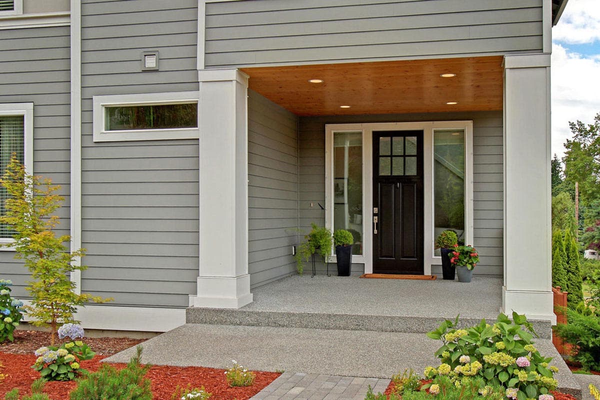 Modern house exterior with covered porch, dark front door, horizontal siding, and a transom window.