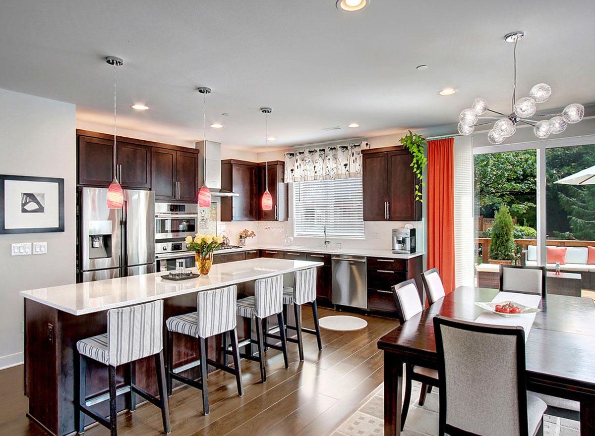 Contemporary kitchen featuring dark wood cabinets, a large island with seating, stainless steel appliances, and an adjacent dining area.