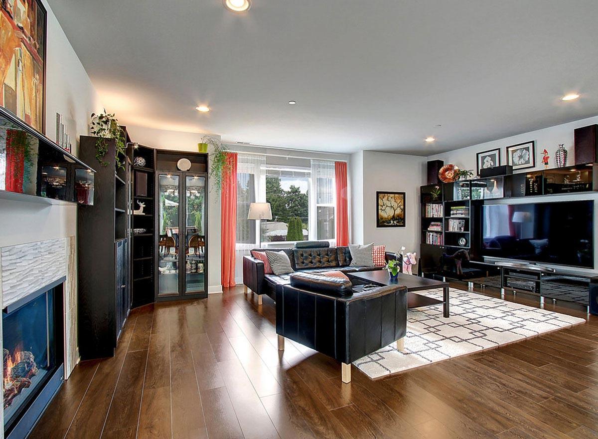 Living room with fireplace, black leather sectional, entertainment center, dark wood floors, and large window with coral curtains.