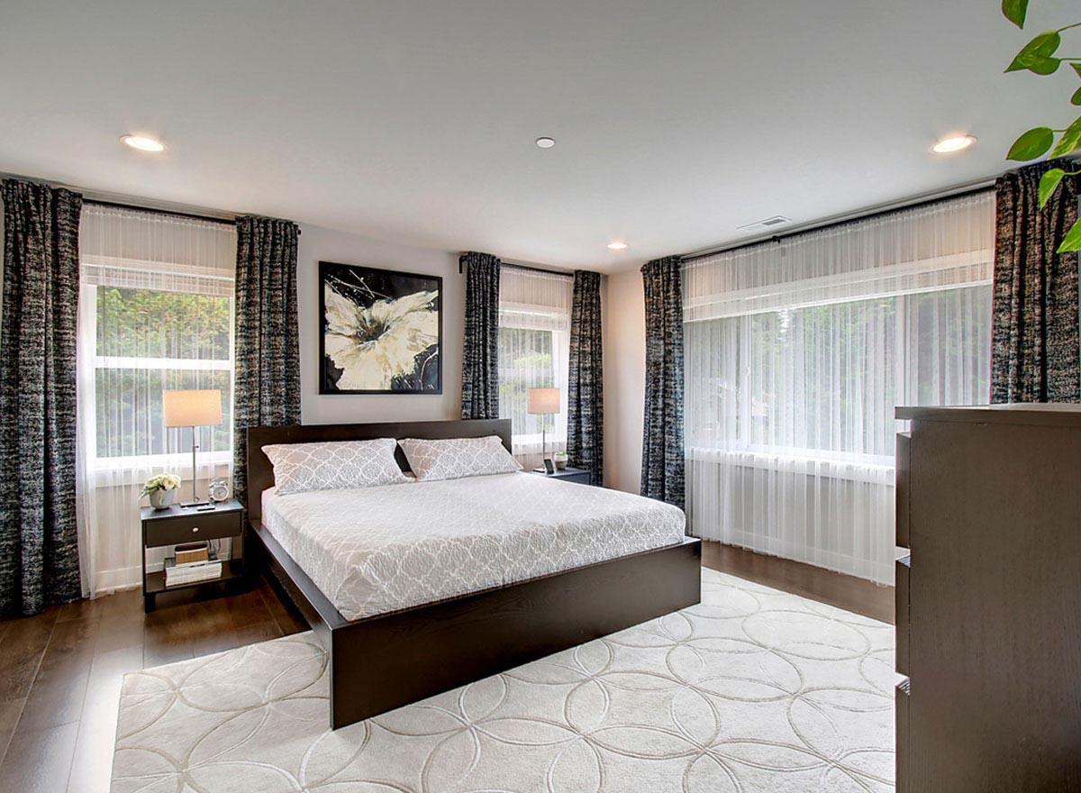 Bedroom with king-size bed, patterned bedding, large windows with dual curtains, and abstract wall art.