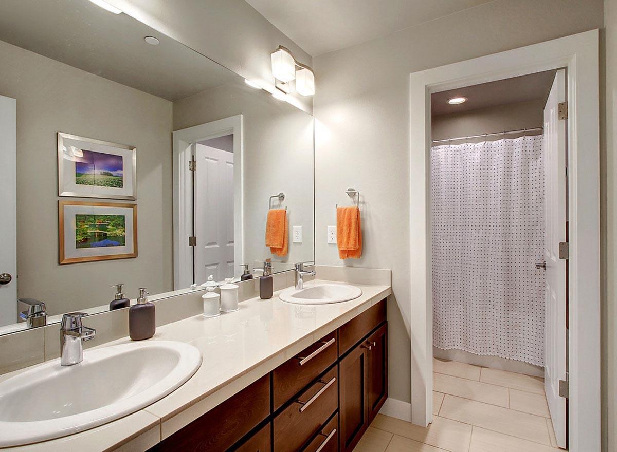 Bathroom with double vanity, wood cabinets, and tiled shower area with polka dot curtain.