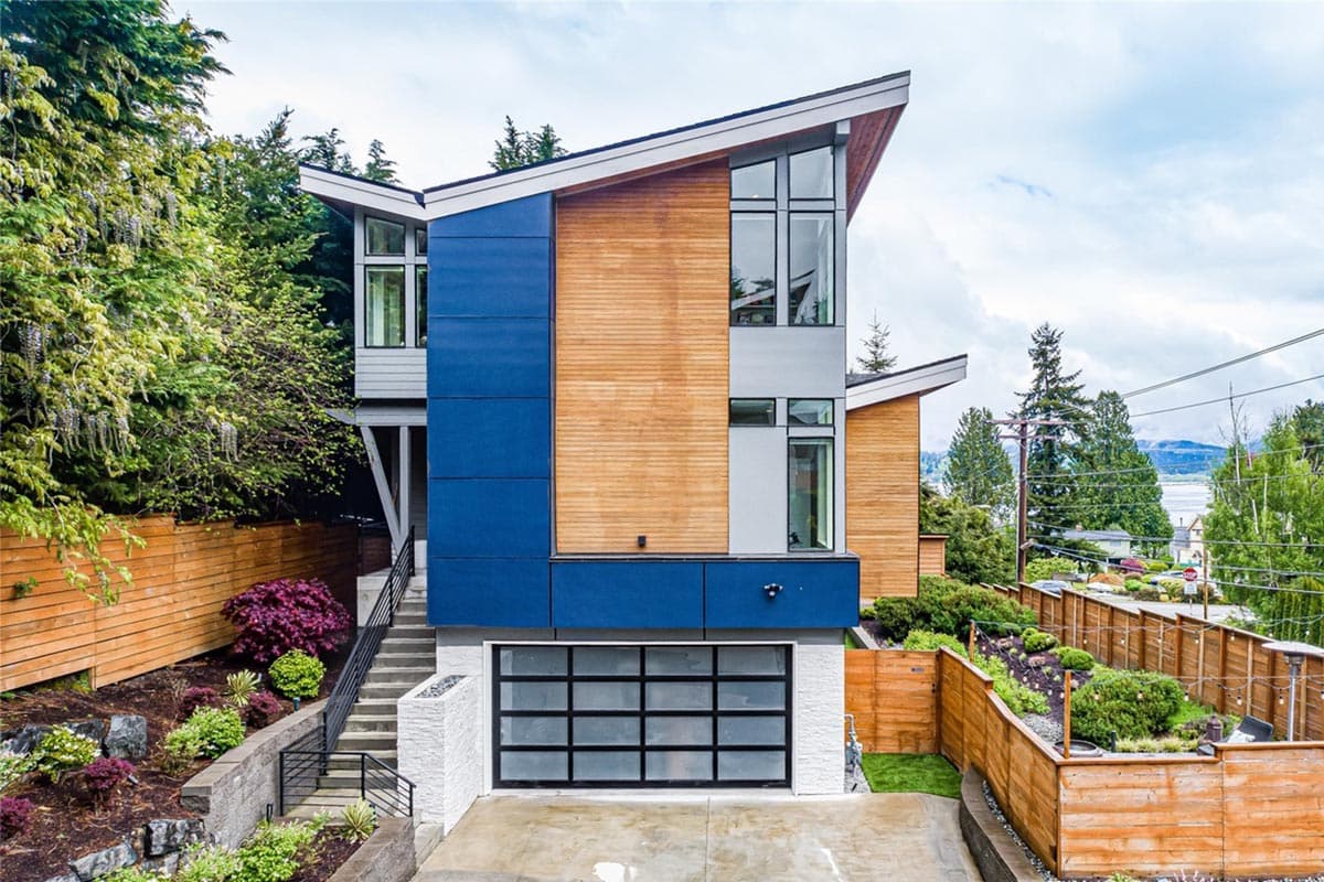 Modern house plan exterior with angled rooflines, wood siding, blue panels, and glass garage door.