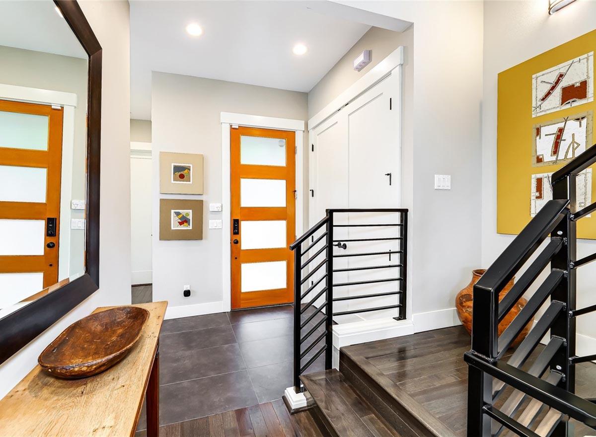 Modern interior foyer with natural wood doors, dark wood floors, and black metal railings leading upstairs.
