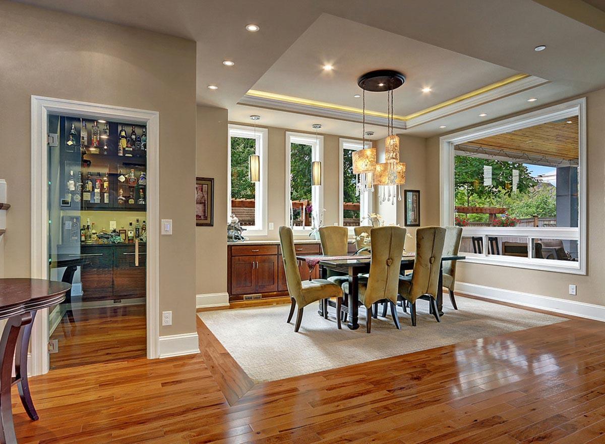Dining room with plush chairs around table, wet bar visible, and large windows overlooking outdoor area. Recessed ceiling detail.