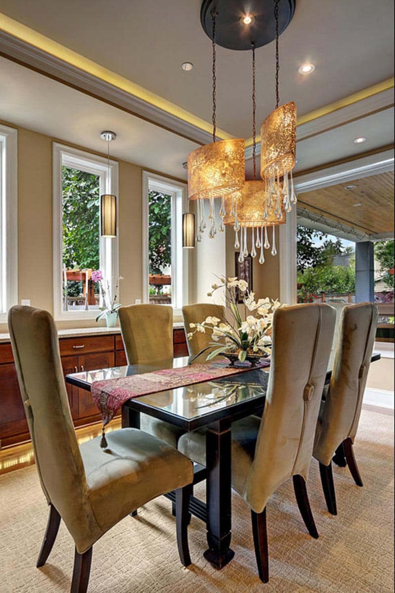 Dining room with dark wood table, upholstered chairs, ornate chandelier, and large windows.