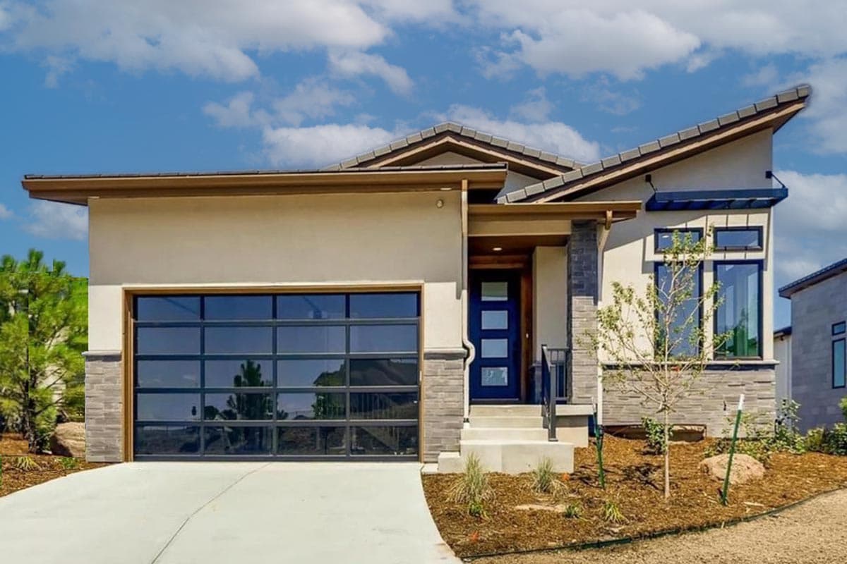 House plan exterior. Modern style, one-story home with glass garage door, angled roof, and stone facade accents around entry and window.