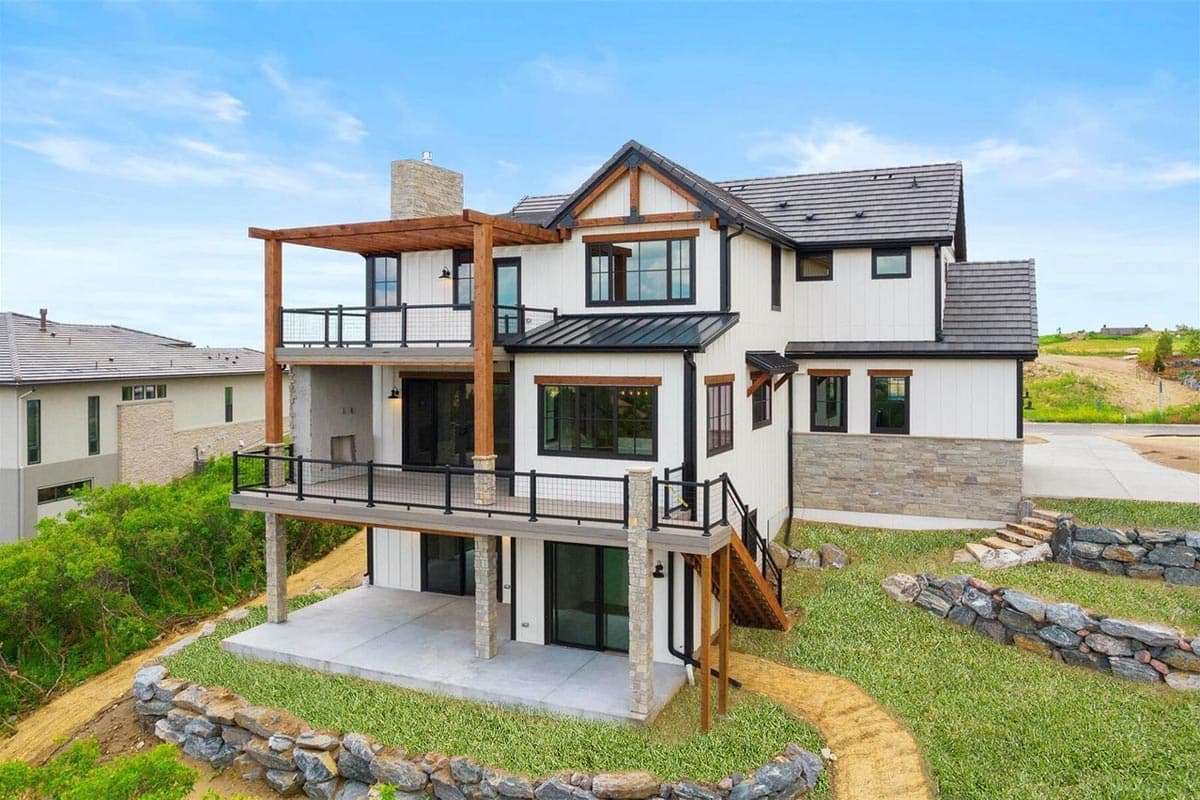 Modern house plan exterior with white board-and-batten siding, stone accents, multiple decks, and a wood pergola.