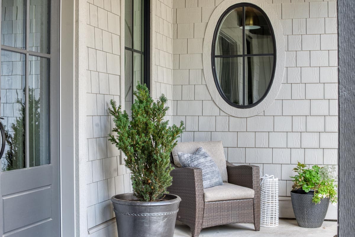 House plan exterior: Light gray shingle siding, front door with glass panes, tall rectangular window, and oval window.