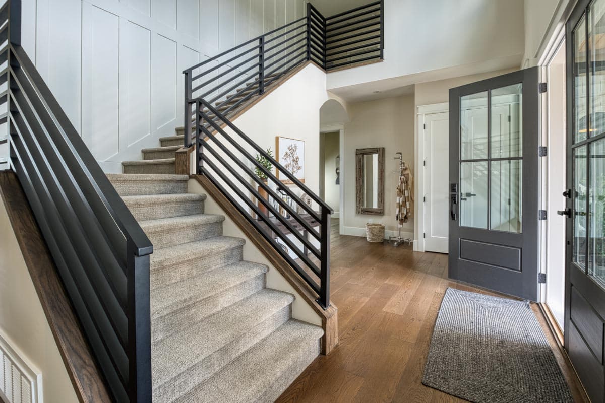 Entryway and staircase with modern black metal railing, carpeted steps, and wood flooring.