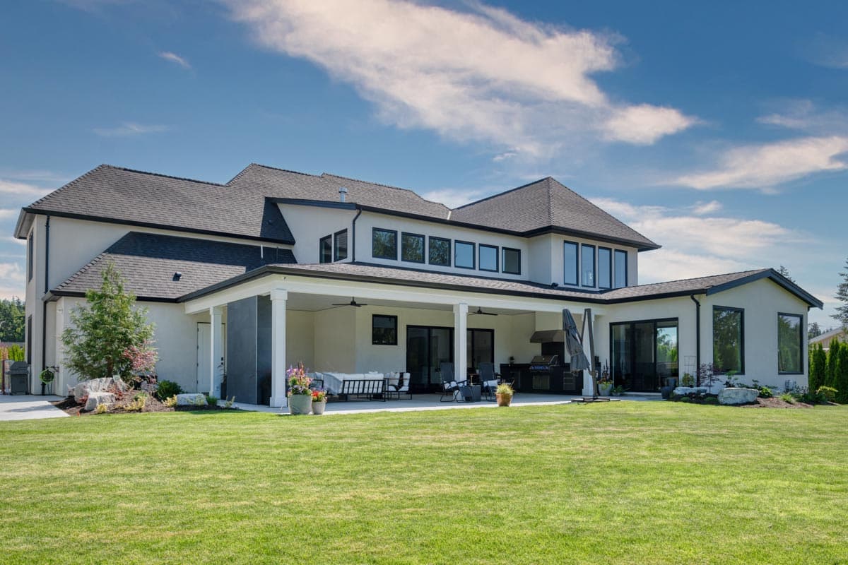 Modern house plan exterior with two stories, covered patio with columns, numerous large windows, and a pitched roof.