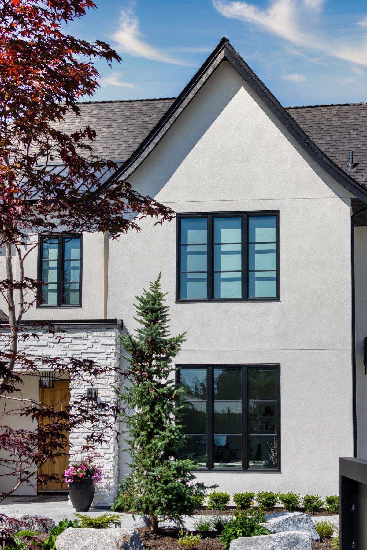 Modern house plan exterior with stucco, stone accent, multiple gables, and large black-framed windows.