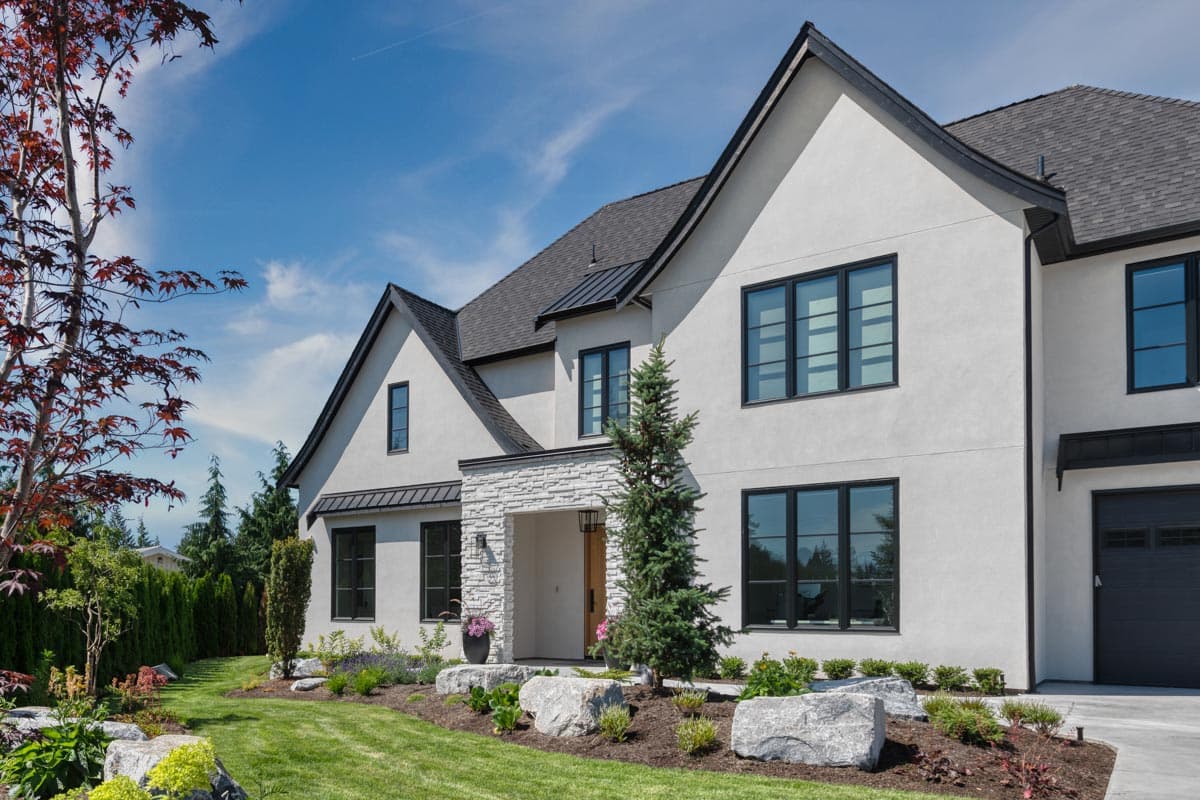 Modern house plan exterior with stucco finish, intersecting gables, stone-clad entryway, and large black-framed windows.