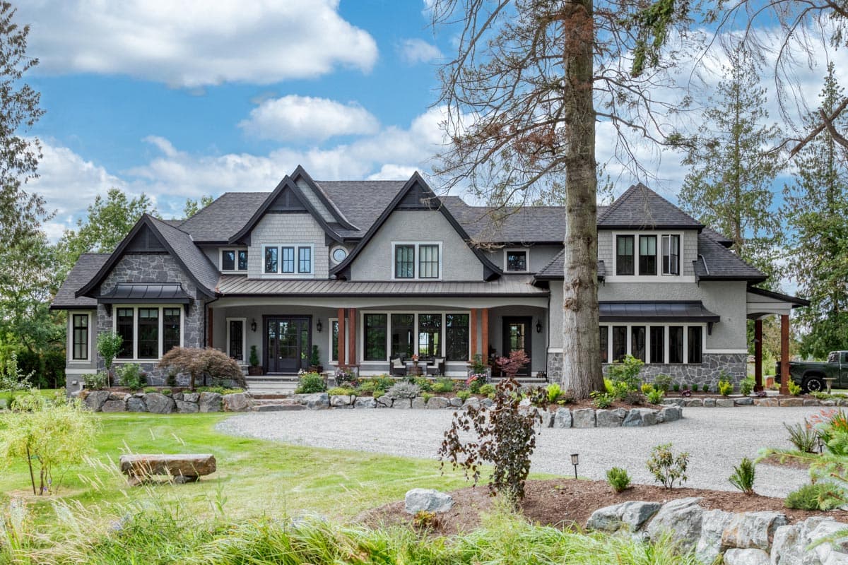 House plan exterior. Two-story Craftsman home with a gabled roof, stone accents, a large covered porch, and multiple dormers.