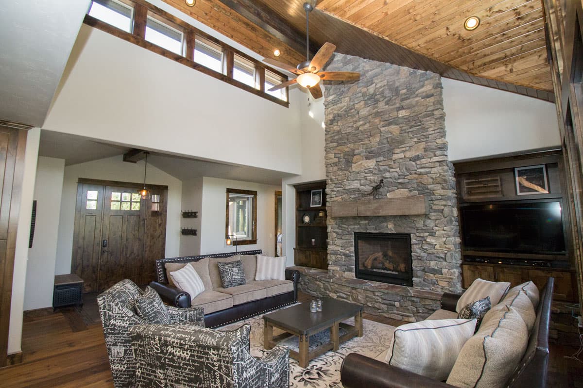 Living room interior with vaulted wood ceiling, stone fireplace, large windows, and wood doors.