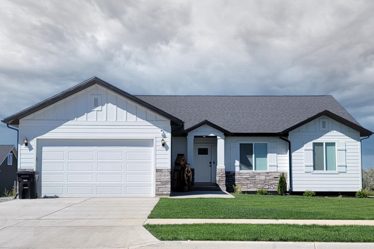 House plan exterior. Ranch style with a two-car garage, gable roof, and stone accents. One story with a front porch entry.