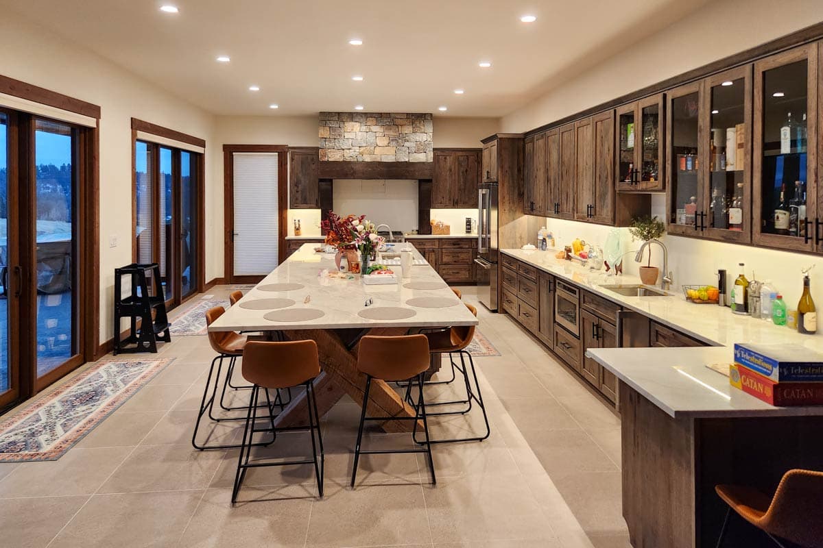 A modern kitchen with a large island and seating. Wooden cabinets line the walls. Large glass doors open to a view outside.